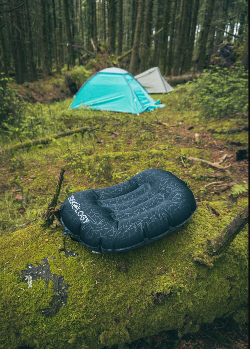 Inflatable camping pillow on a mossy ground with tents in the background